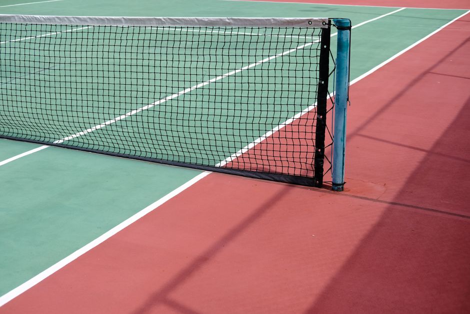 Detailed view of a tennis net on a vibrant outdoor court with sunlight and shadows.